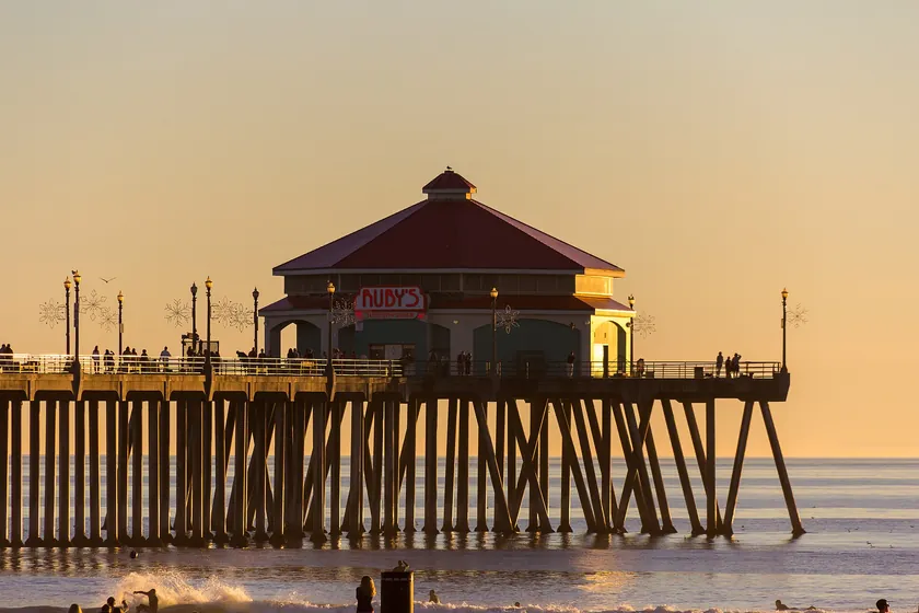 Huntington Beach Pier at sunset, its pilings and the restaurant pavilion at the end silhouetted against a golden sky