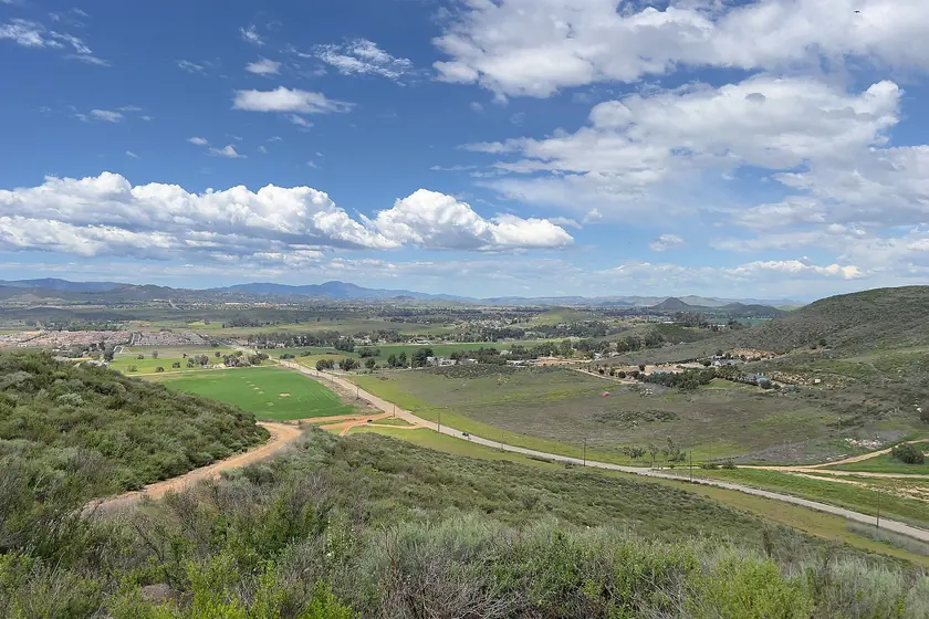 Green fields and rolling chaparral hills stretching across the valley toward Menifee under a sky of scattered clouds