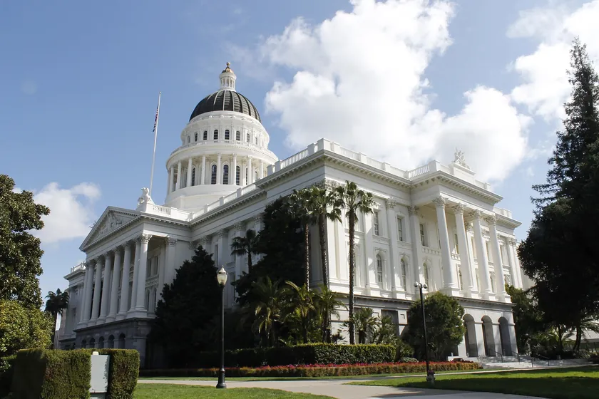 The California State Capitol's white dome and columned front among the trees of Capitol Park in Sacramento