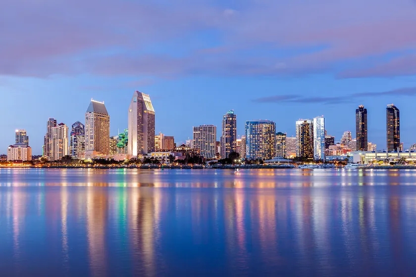 Downtown San Diego's skyline lit at dusk and reflected in the still water of San Diego Bay