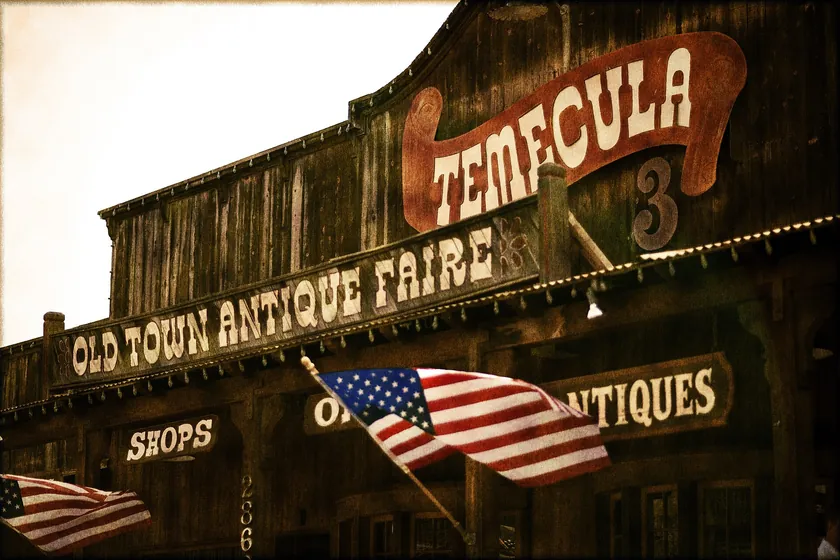 The weathered wooden storefront of the Old Town Antique Faire, hung with American flags, in Old Town Temecula